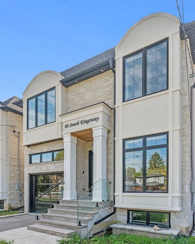 Modern two-story house with cream and stone facade, curved glass windows, and metal railings at 80 South Kingsway