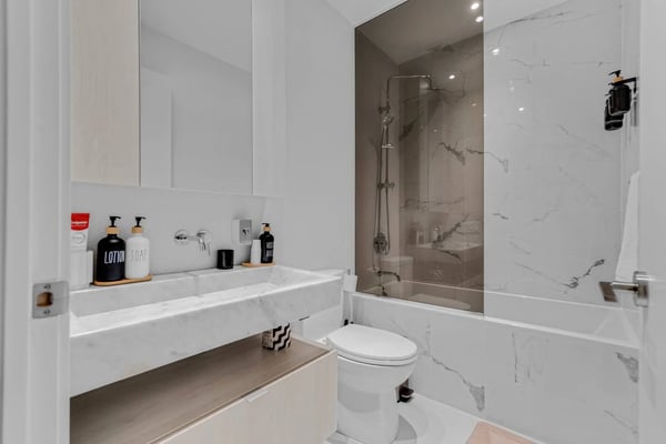 Modern bathroom with white marble walls, floating vanity with sink, toilet, and glass-enclosed shower with rainfall showerhead.