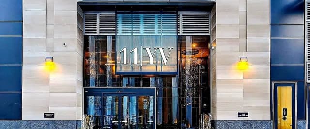 Modern building entrance with glass canopy, blue and white facade, and illuminated signage reading 11W